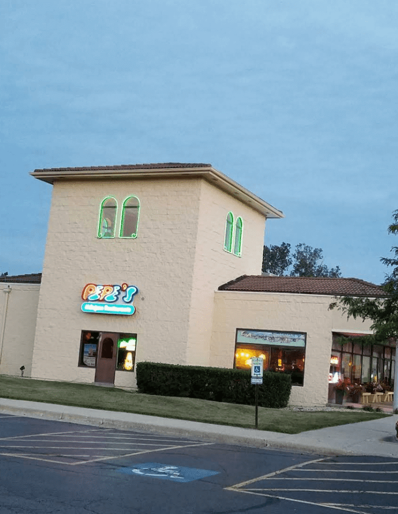 Exterior view of Pepe’s Mexican Restaurant with arched entrance, brick details, and colorful logo sign above the door.