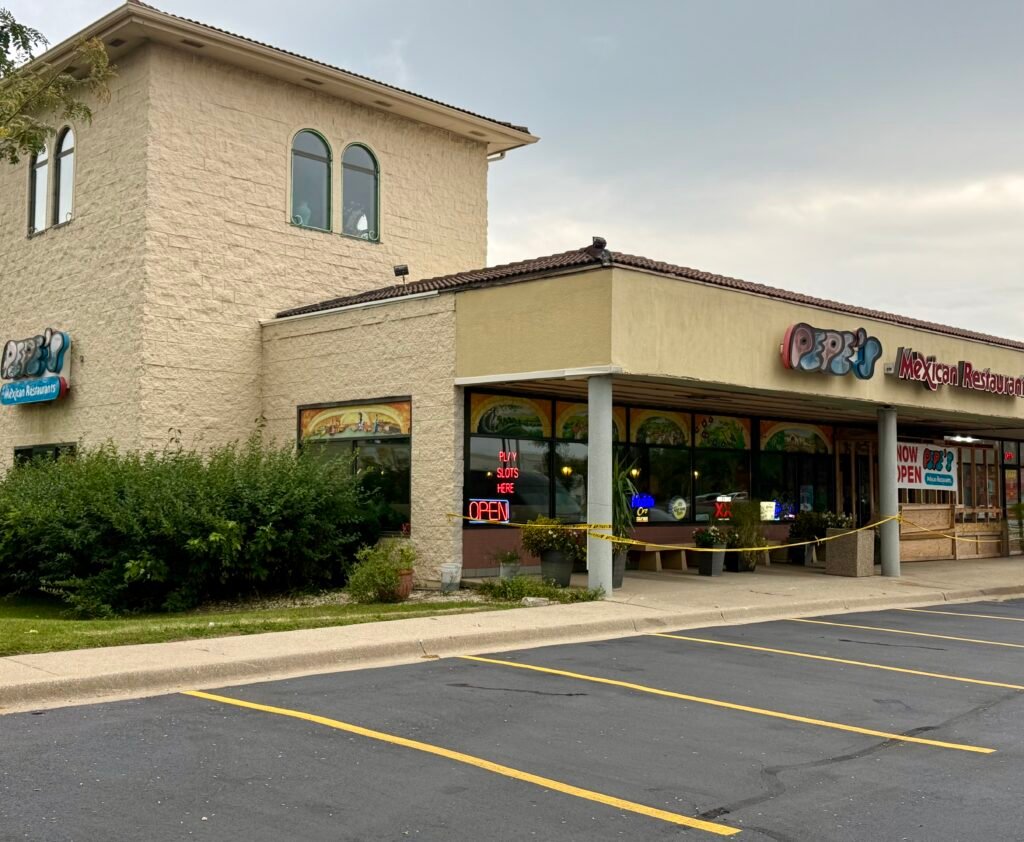 Exterior of Pepe’s Mexican Restaurants & Cantina with brick wall, colorful logo sign, and neon OPEN light in the window.